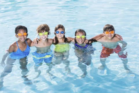 Multi-ethnic group of children having fun in swimming pool. Ages 9 to 13.