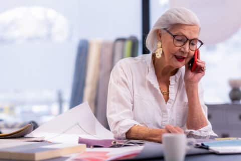 older woman sitting at desk, on the phone and working