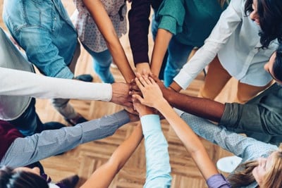 Numerous individual's arms meeting together with hands in the middle stacking on top of each other