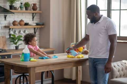 Table disinfection. African american tall bearded man spraying disinfector on the table surface